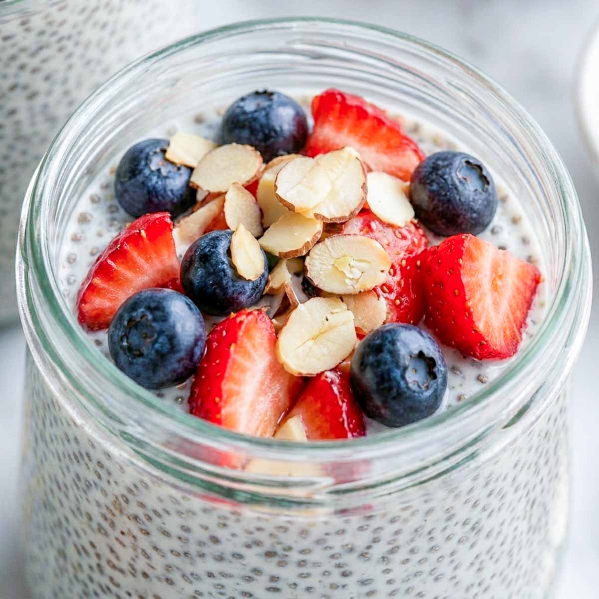 Close up of a jar of kefir chia pudding topped with berries and nuts.