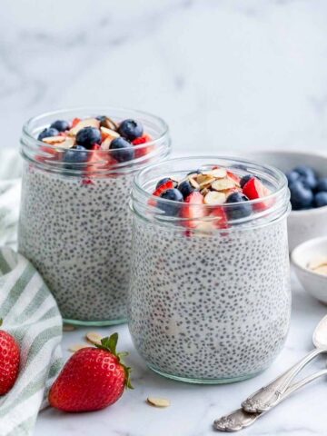 Two glass jars of high protein kefir chia pudding topped with strawberries, blueberries, and sliced almonds.