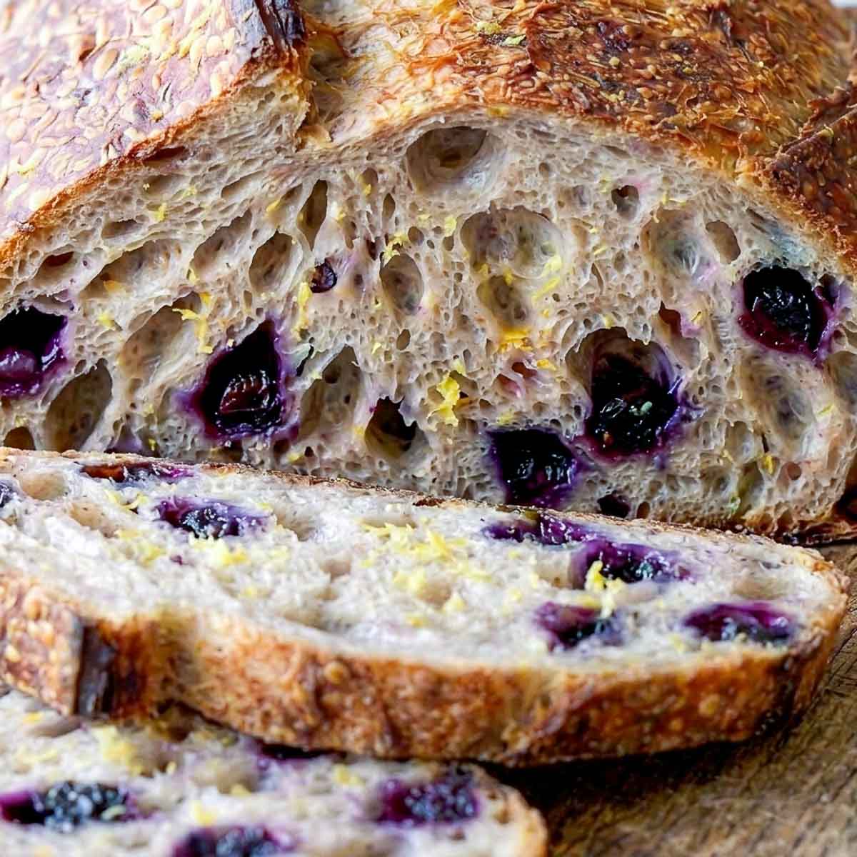 Close-up of lemon blueberry sourdough bread crumb with burst blueberries and lemon zest flecks.