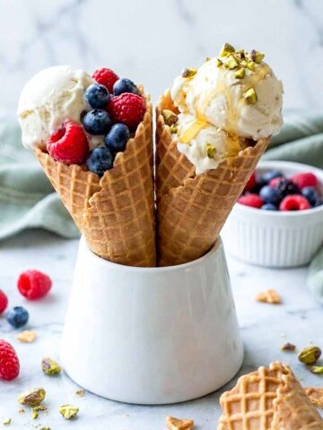 Two waffle cones of no churn kefir ice cream topped with berries, pistachios and honey.