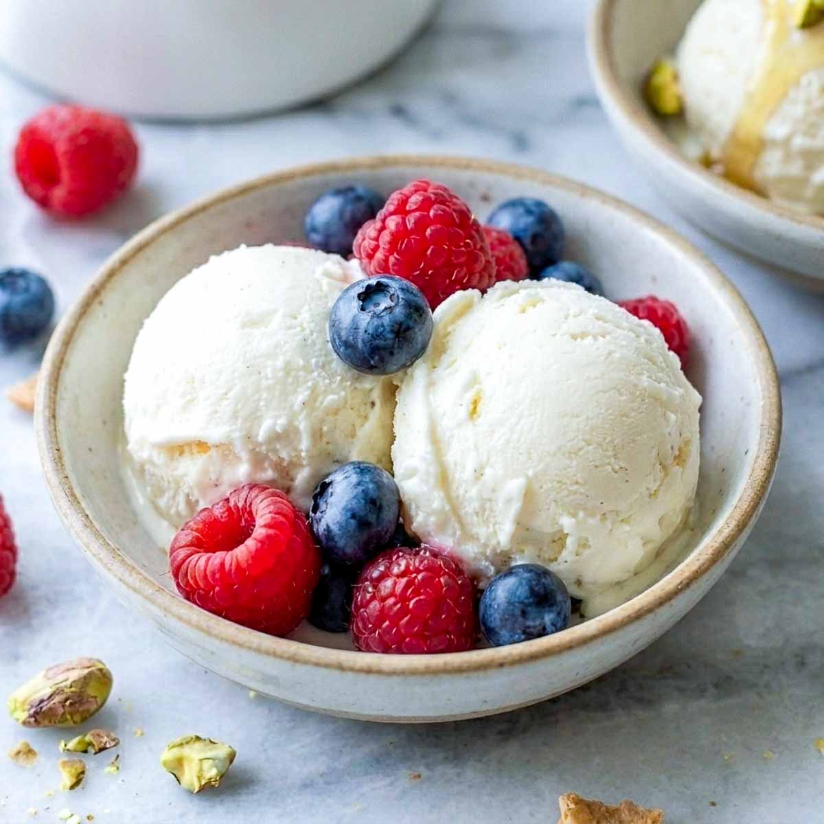 Scoops of kefir ice cream in a shallow bowl with fresh raspberries and blueberries.