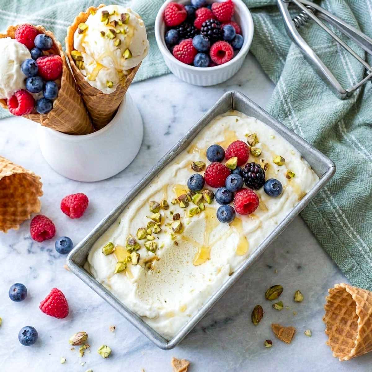 Overhead view of no churn kefir ice cream in a loaf pan beside waffle cones and a bowl of berries.