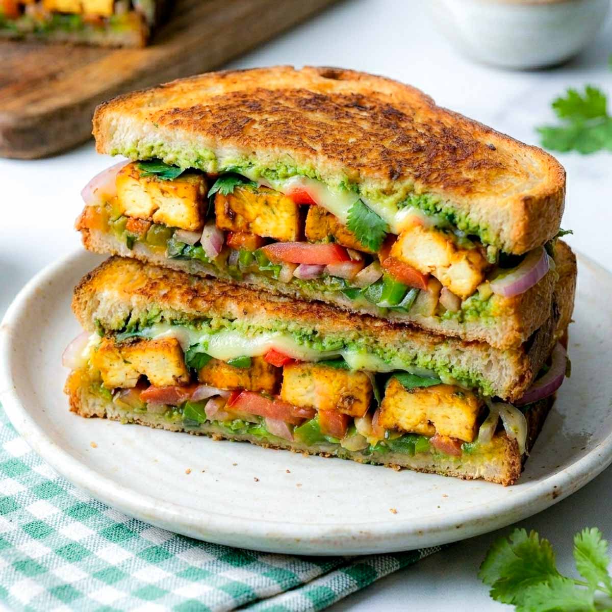 Close-up of a paneer sandwich placed on a white plate with wooden board in the background.