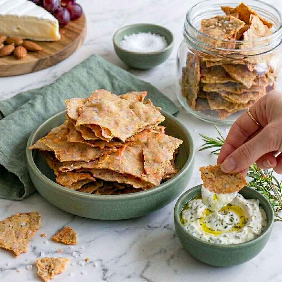 Hand dipping a sourdough discard cracker into herbed yogurt dip.