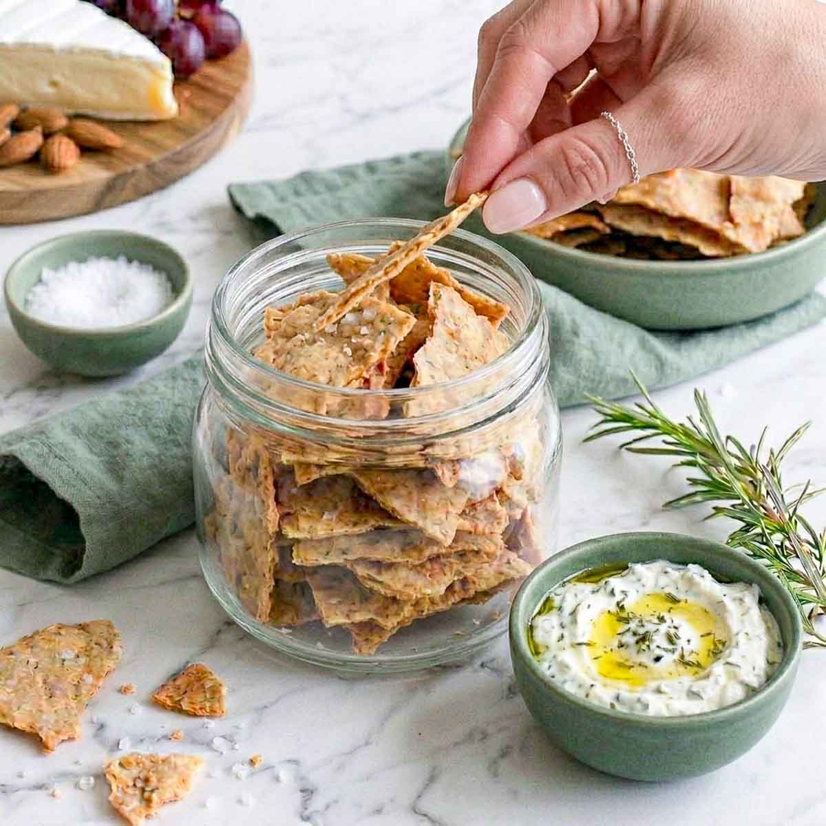 Woman holding a sourdough cracker from the jar showing the thickness of the cracker.