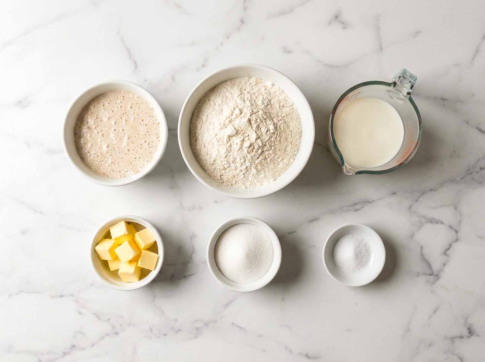 Sourdough starter, all purpose flour, milk, butter, sugar and salt in bowls for sourdough sandwich bread.