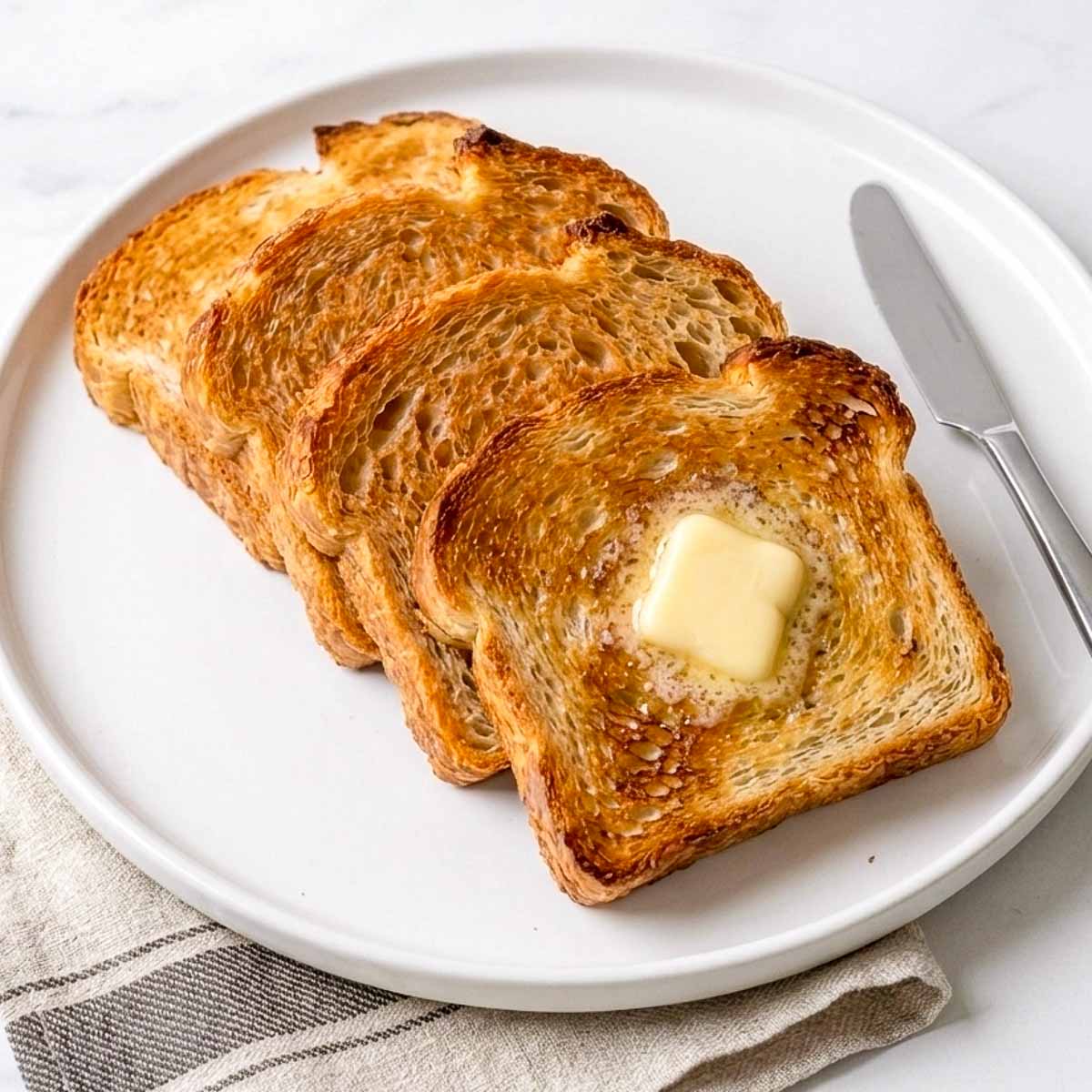 Toasted slices of sourdough sandwich bread on a white plate with melting butter.