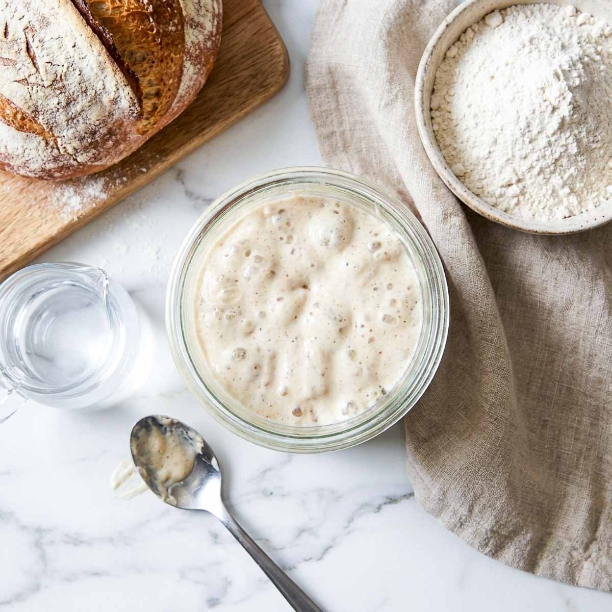 Overhead view of a bubbly sourdough starter in a jar with flour and water.