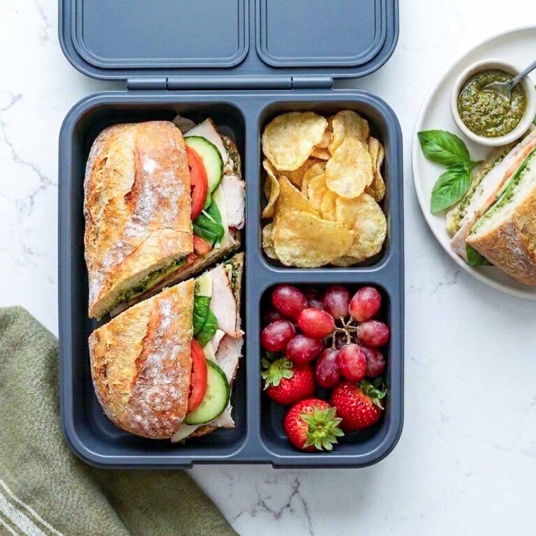 Turkey pesto baguette placed in a lunchbox along with fruits.