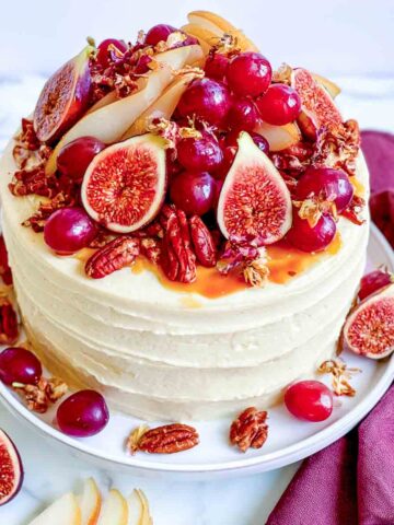 Festive autumn layer cake topped with fresh figs, cranberries, sliced pears, pecans, and dried flowers over creamy frosting.