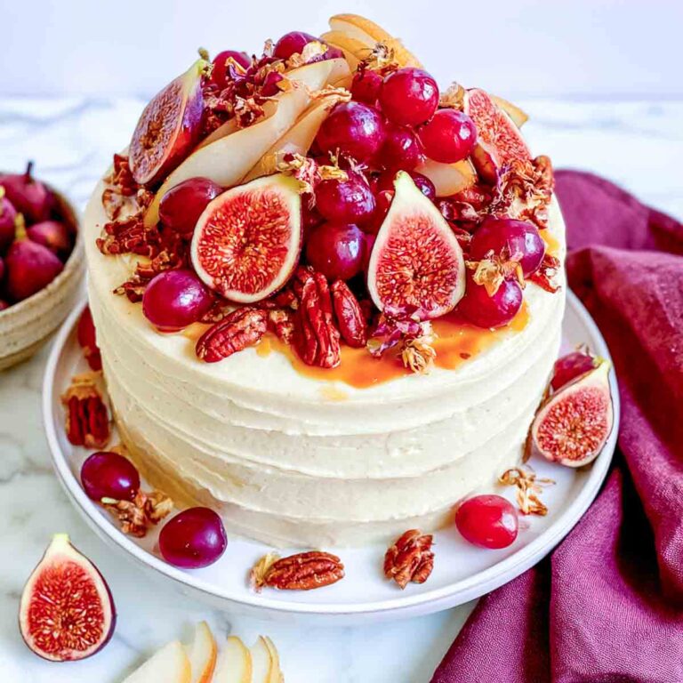 Festive autumn layer cake topped with fresh figs, cranberries, sliced pears, pecans, and dried flowers over creamy frosting.