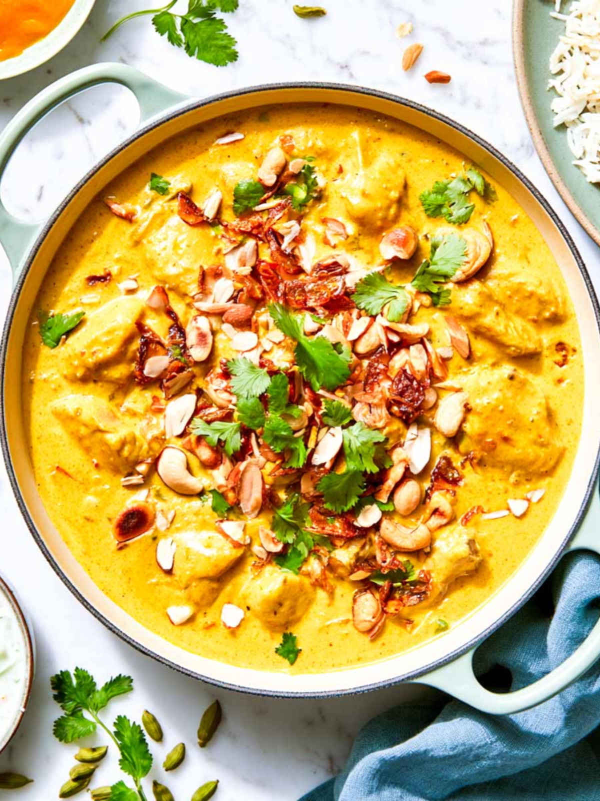 Creamy chicken korma in a pale green braiser topped with crispy fried onions, cashews, and cilantro.