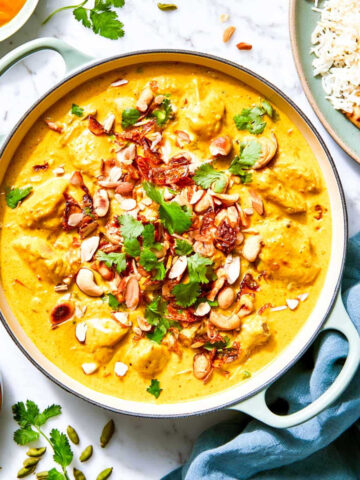 Close up of chicken korma in a pale green braiser topped with crispy fried onions, cashews, and cilantro.