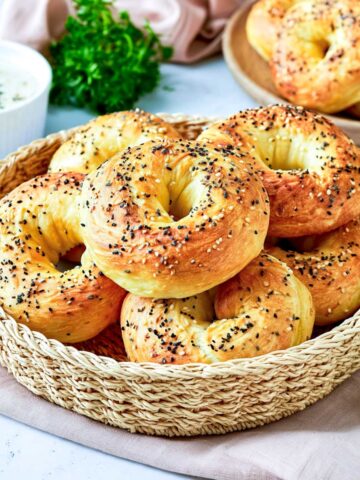 Golden cottage cheese bagels topped with everything bagel seasoning, piled in a woven basket with a small bowl of creamy dip in the background.