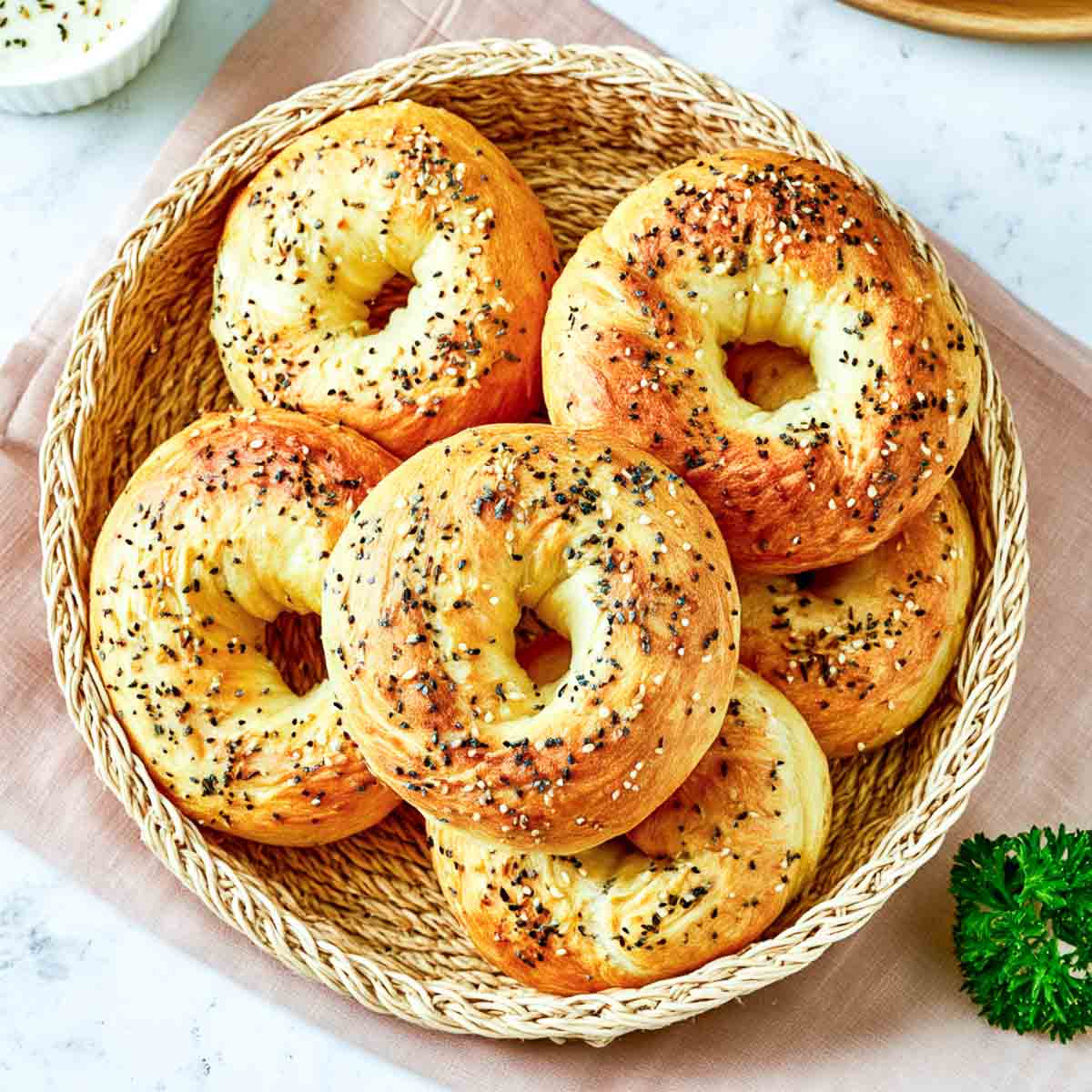 Homemade cottage cheese bagels topped with everything seasoning, arranged in a woven basket on a white marble surface.