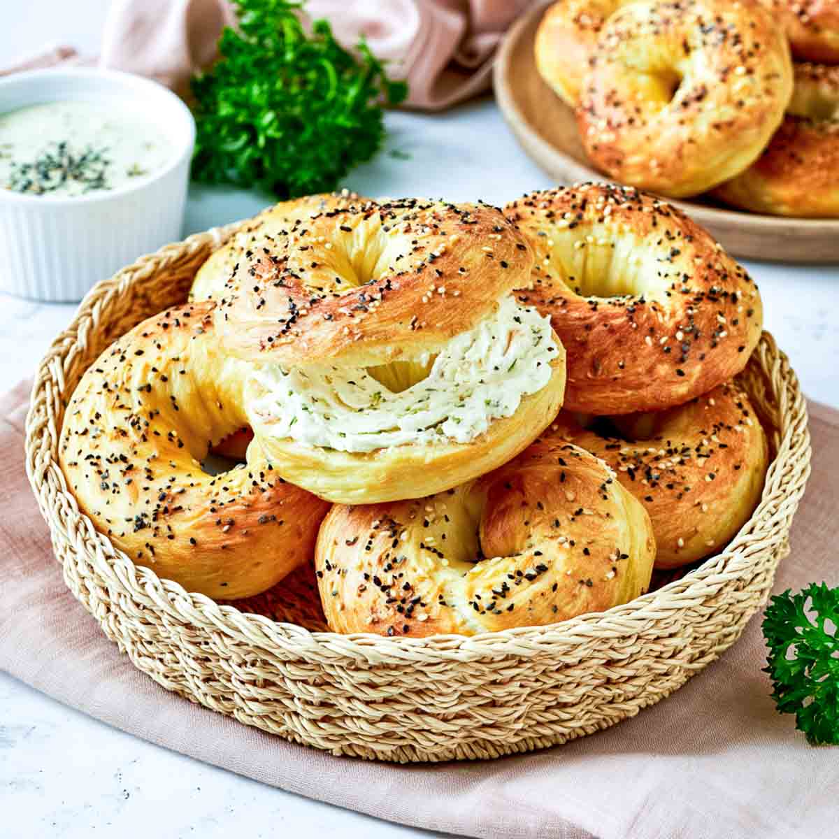 Cottage cheese bagel sliced and spread with creamy herb cream cheese, resting on a basket of golden everything-seasoned bagels.