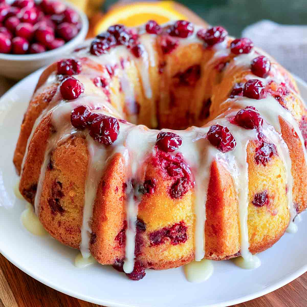 Cranberry orange Bundt cake drizzled with white glaze and topped with fresh cranberries and orange slices.