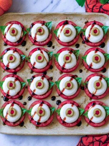 Eyeball caprese bites made from tomato slices, basil, and cheese rounds topped with pimento stuffed olive slices.