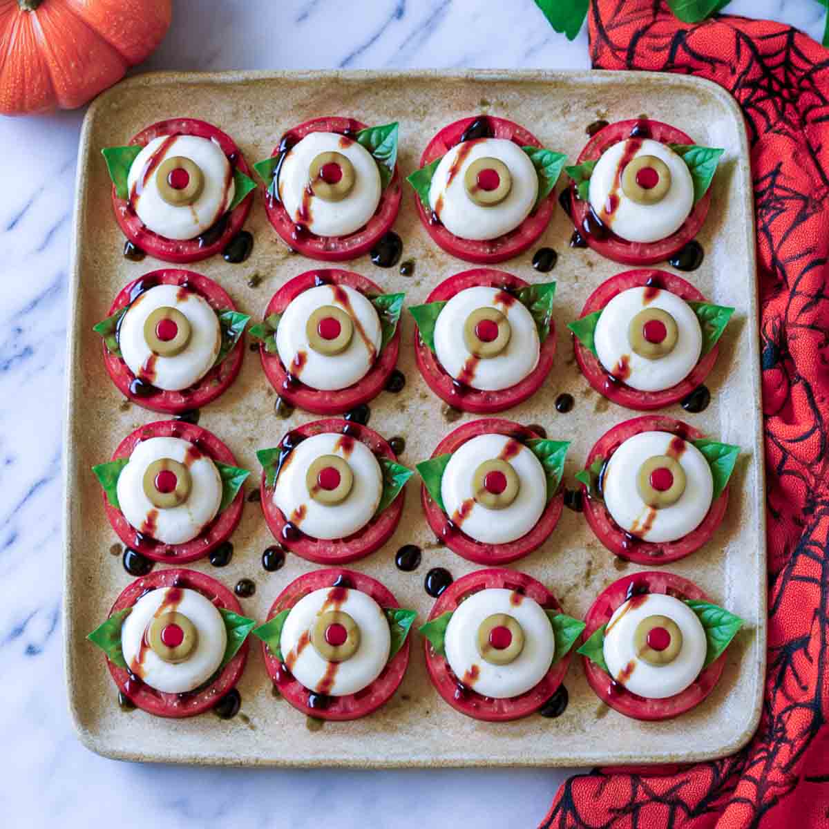 Eyeball caprese bites made from tomato slices, basil, and cheese rounds topped with pimento stuffed olive slices.
