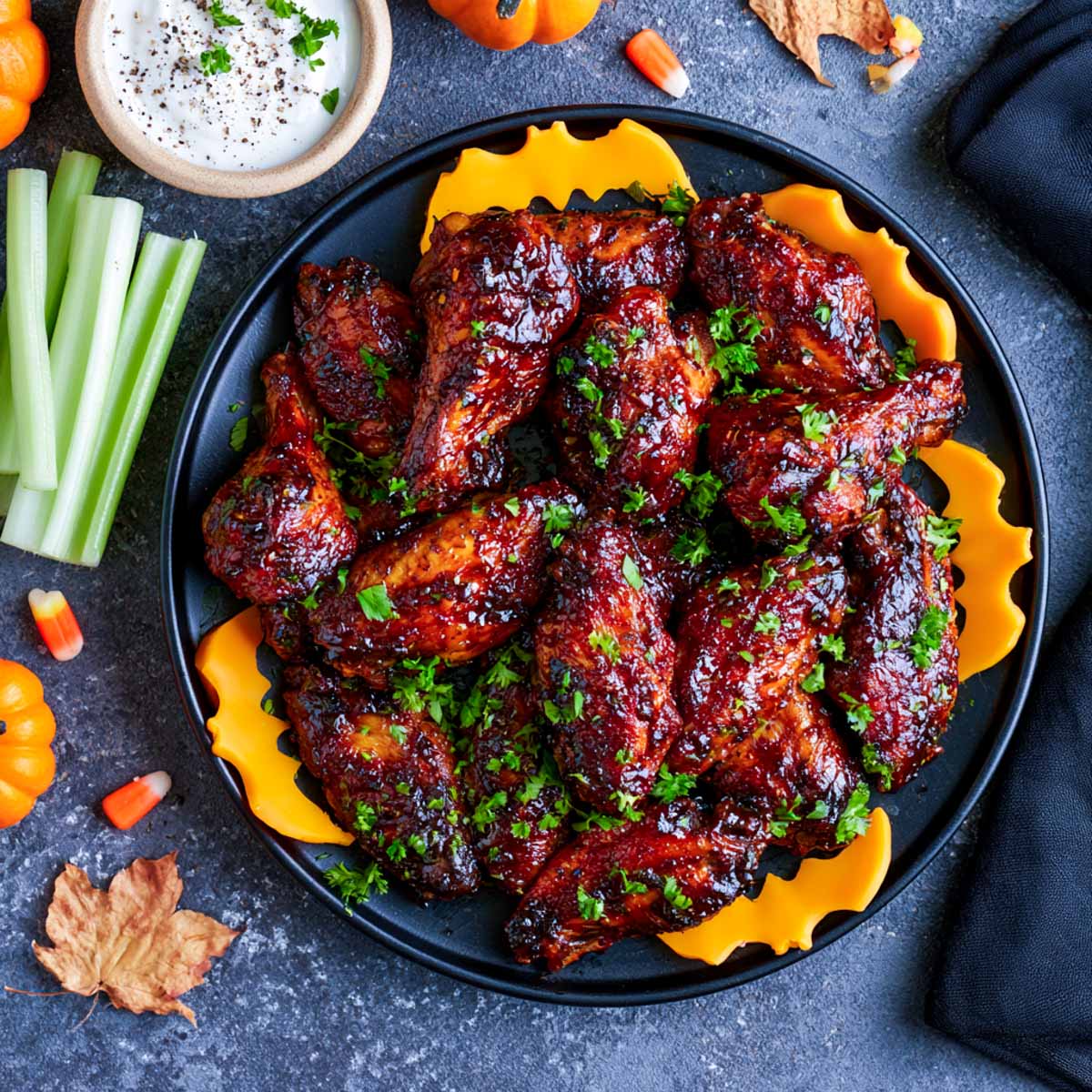 Platter of Halloween bat wings in dark sticky glaze with orange bell pepper bats, celery sticks and ranch dip.