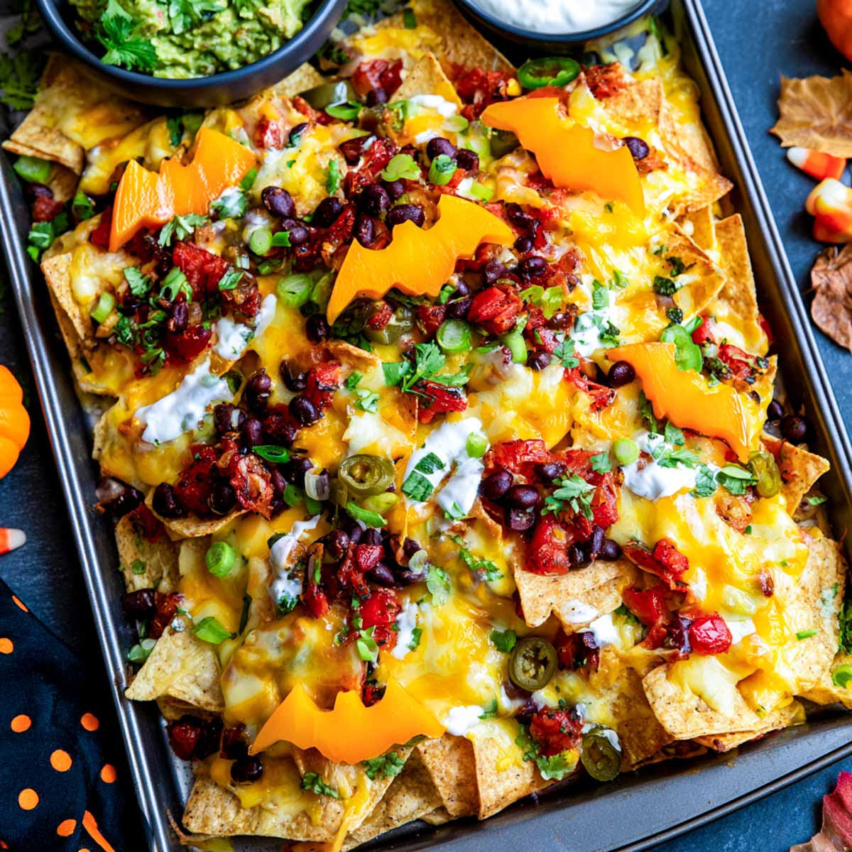 Sheet pan of Halloween nachos with melted cheese, black beans and orange bell pepper bats scattered across the top.