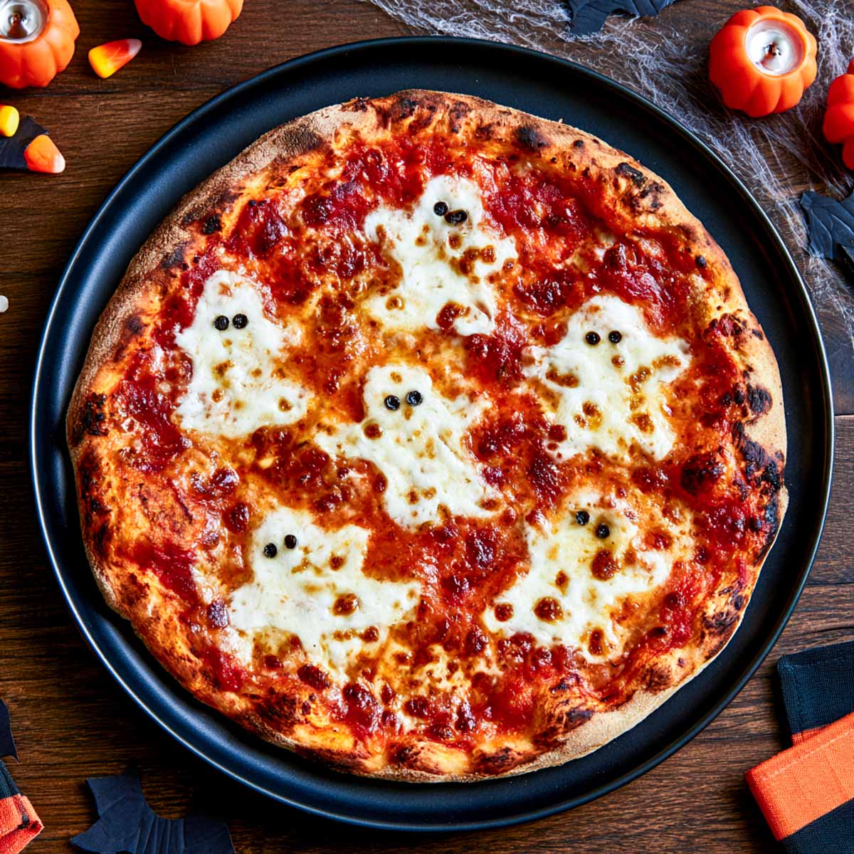 Halloween ghost pizza with mozzarella cut into ghost shapes on red sauce with small black olive eyes.