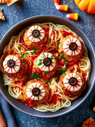 Bowl of Halloween spaghetti topped with meatballs decorated as eyeballs with mozzarella rounds and sliced olives.