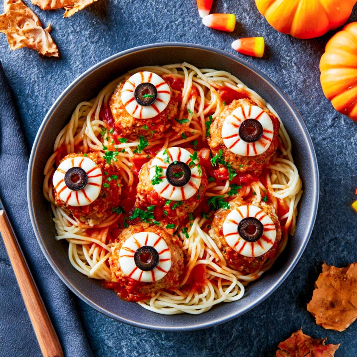 Bowl of Halloween spaghetti topped with meatballs decorated as eyeballs with mozzarella rounds and sliced olives.