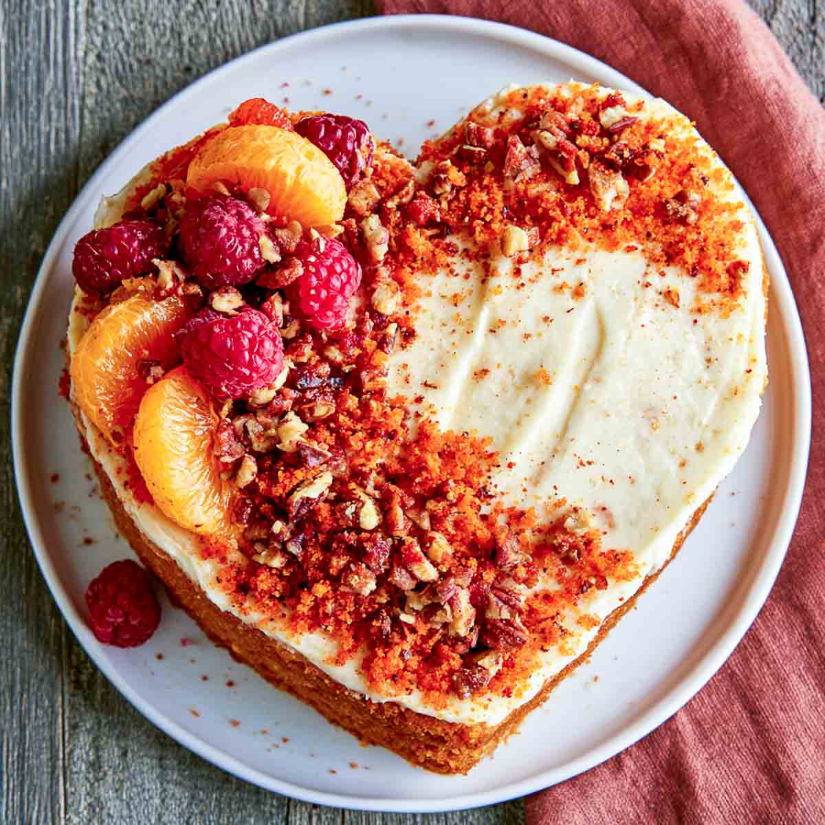Heart-shaped Friendsgiving cake covered with cream cheese frosting and topped with raspberries, mandarin oranges, chopped nuts, and crumb topping.