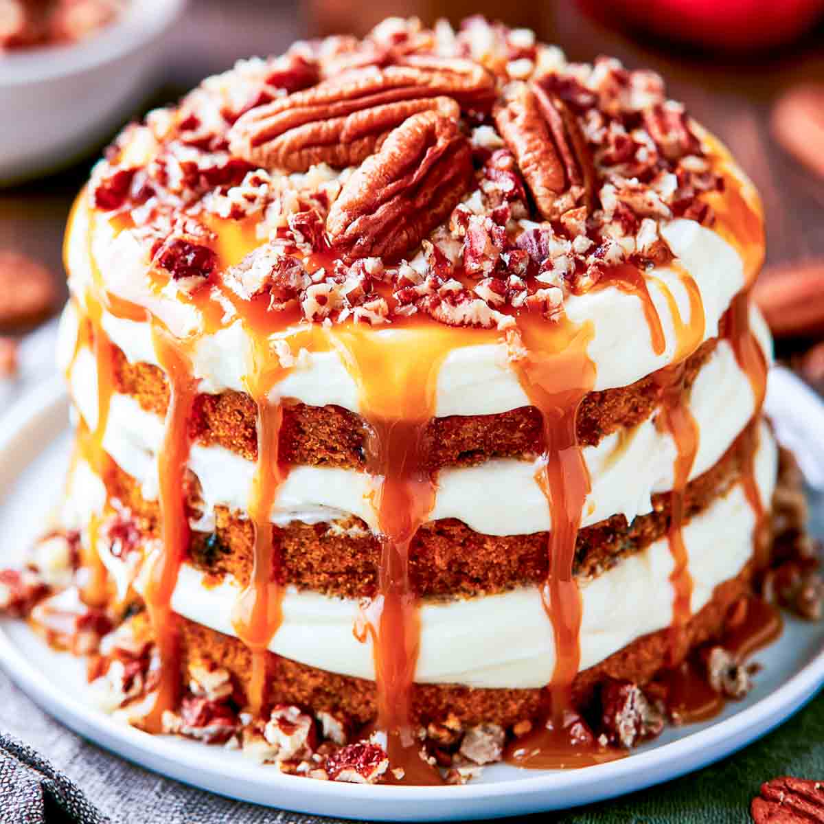 Layered pumpkin cake with cream cheese frosting, caramel drizzle, and chopped pecans between and over the cake layers.