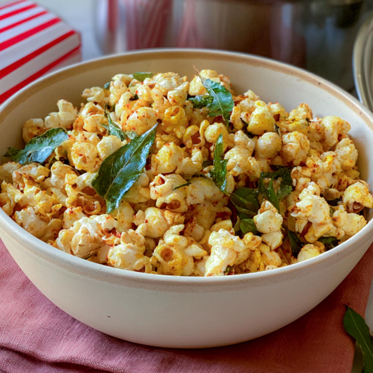 Close view of masala popcorn showing whole crisped curry leaves and red chili flecks clinging to the popped corn.
