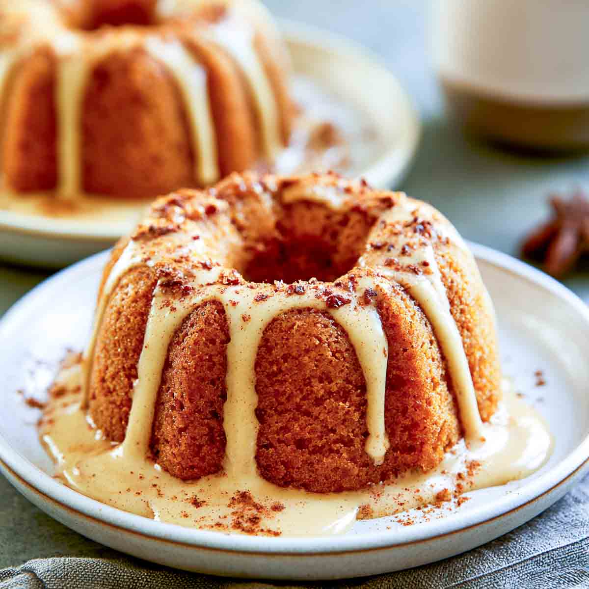 Pumpkin spice Bundt cake topped with creamy coffee-colored glaze and a dusting of cinnamon, served on a ceramic plate.