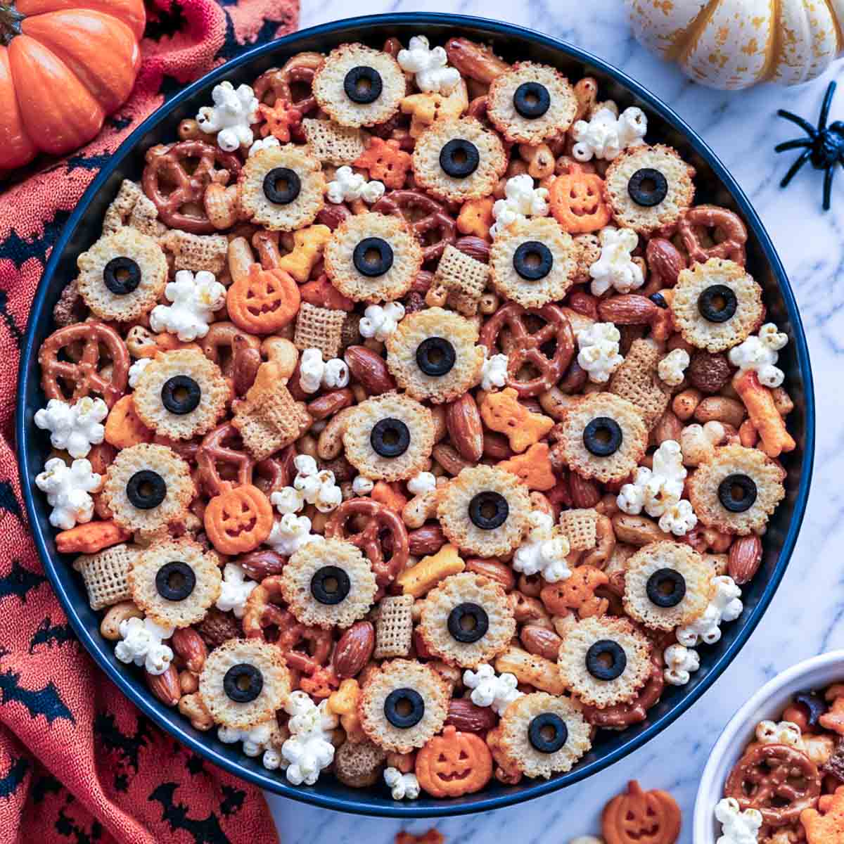 Savory Halloween snack mix with Parmesan crisp eyes, pretzels, popcorn, and pumpkin shaped cheese crackers in a black bowl.