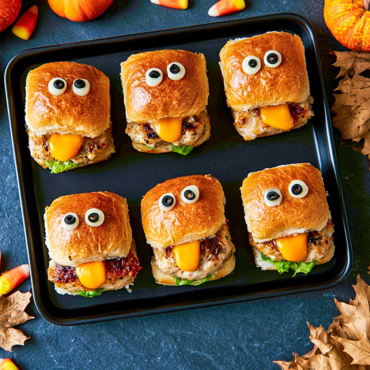 Six Halloween monster sliders with mozzarella and olive eyes and cheese slices hanging out like tongues.