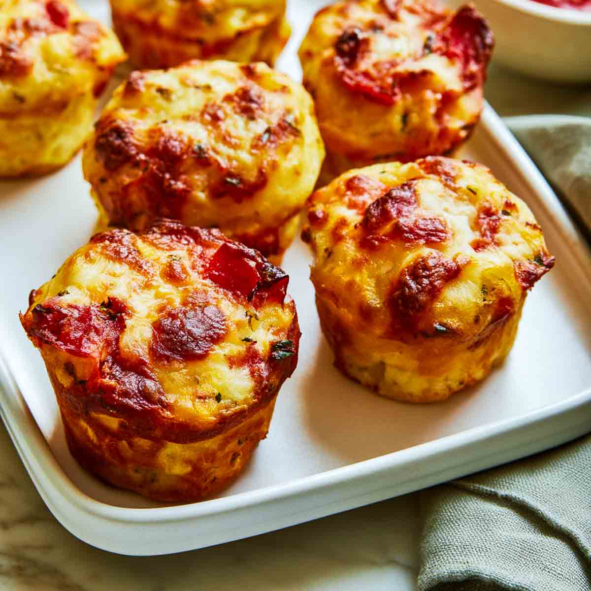 Close-up view of cheesy pizza muffins topped with pepperoni and baked until golden brown, arranged on a white serving tray.