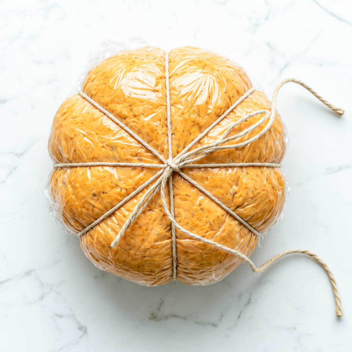 Plastic-wrapped cheese ball tied with kitchen twine into pumpkin ridges before chilling.