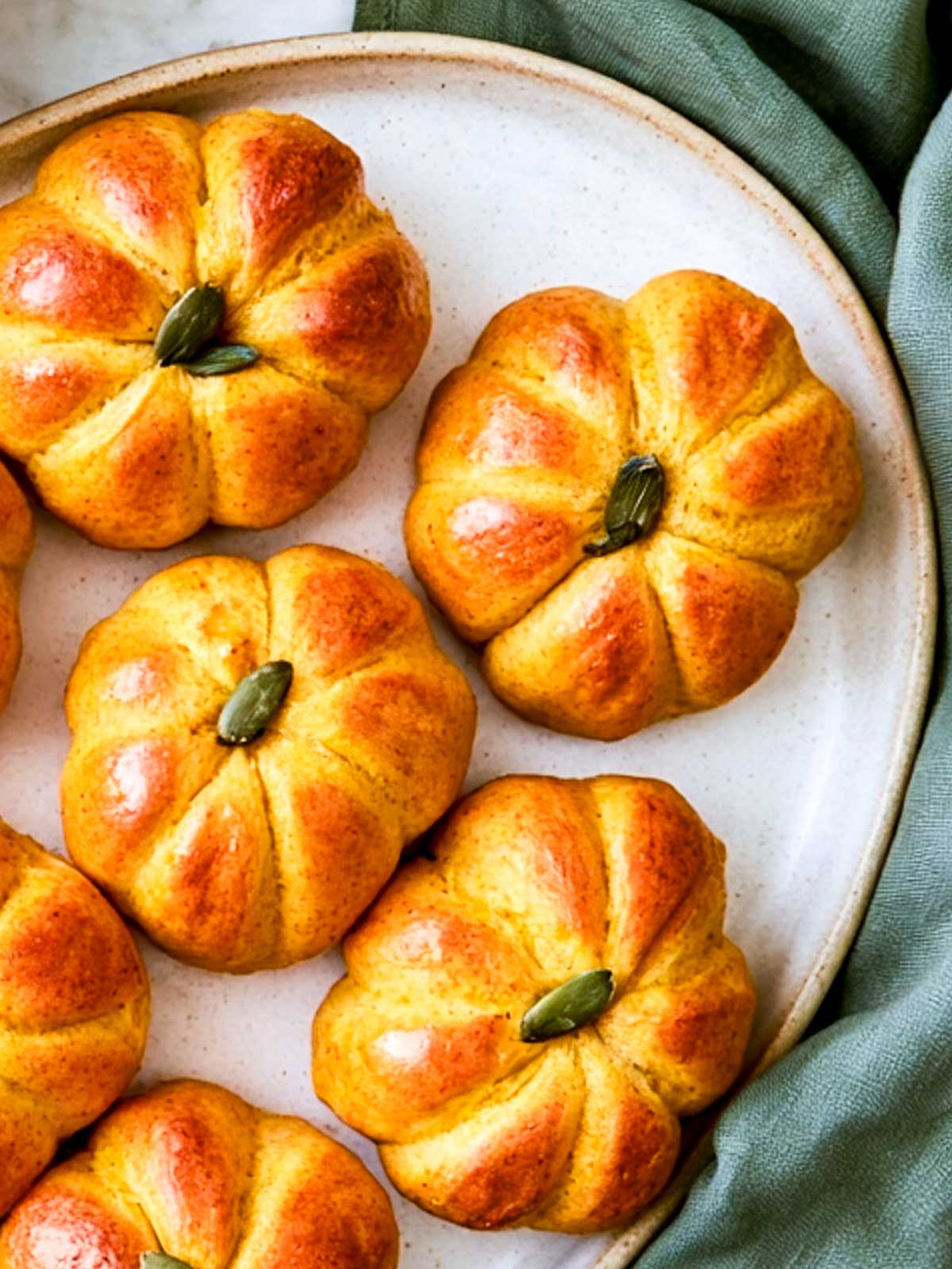 Close-up of pumpkin-shaped bread rolls placed on a white serving plate.