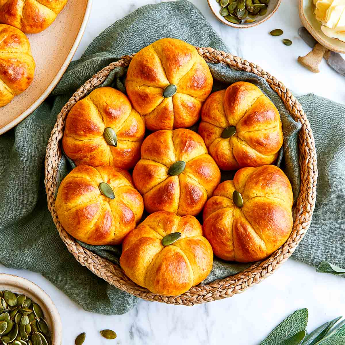 Seven pumpkin-shaped bread rolls nestled in a woven basket lined with a green linen napkin.