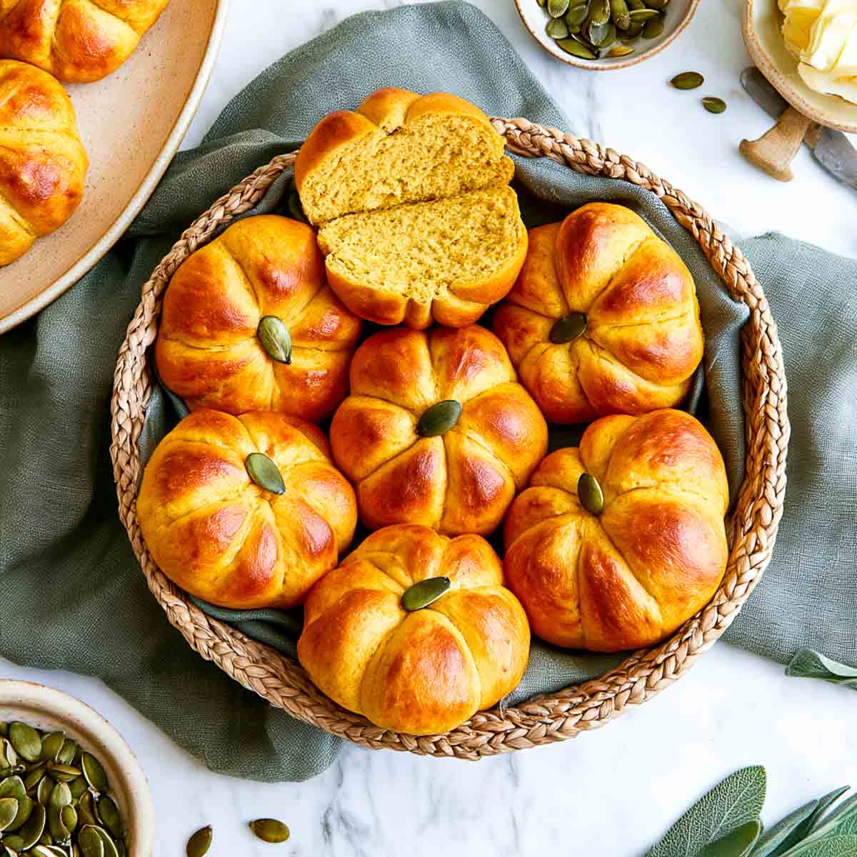 A pumpkin-shaped roll split open to show the soft golden crumb, resting on more rolls in a basket.