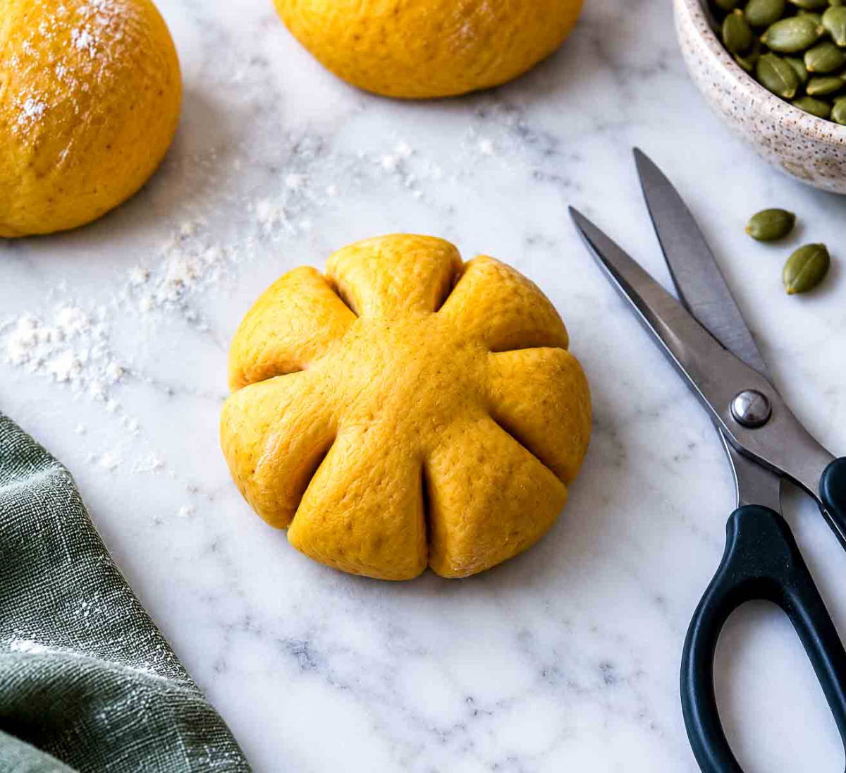A flattened disk of pumpkin dough cut into eight lobes with kitchen scissors on a floured marble surface.