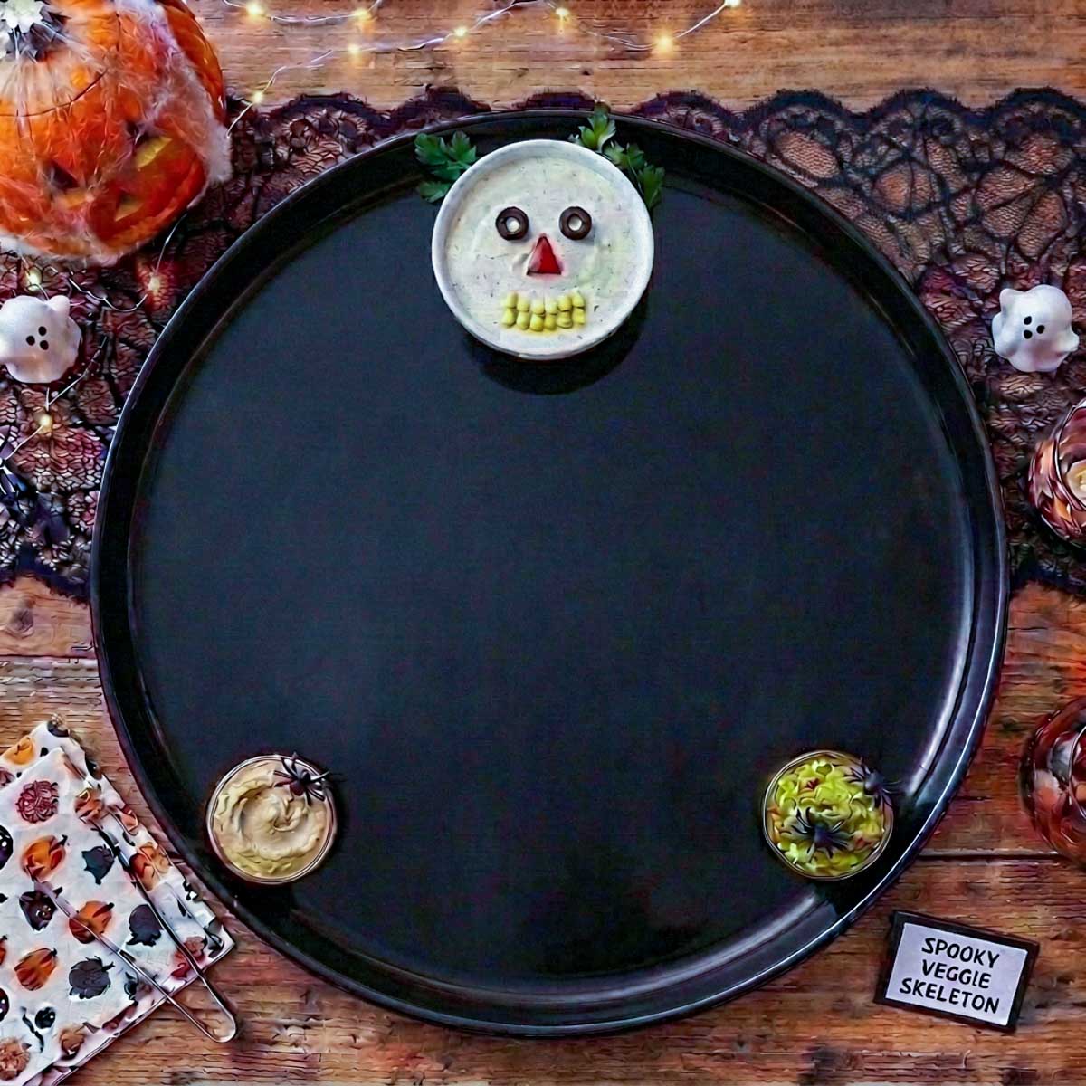  Empty black Halloween platter with a bowl of ranch dip decorated as a skull face and two smaller dip bowls at the bottom.