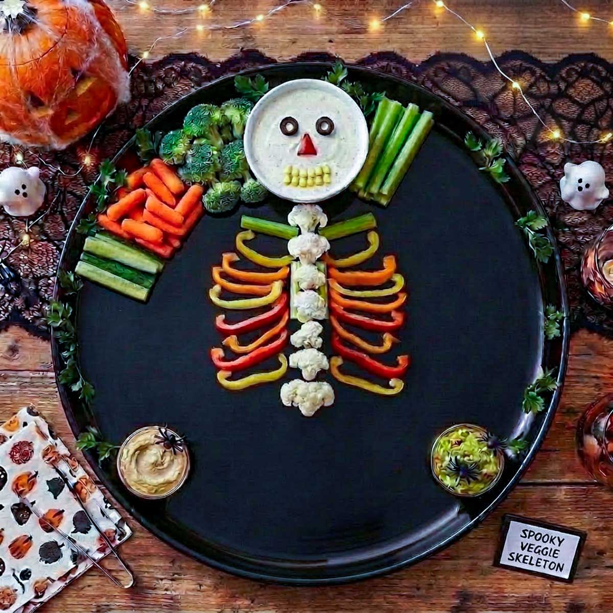 Cauliflower spine with red, yellow, and orange bell pepper ribs arranged on a black Halloween platter.