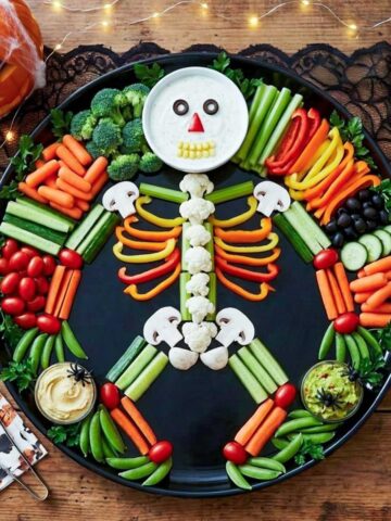 Halloween veggie tray arranged as a skeleton on a black platter with a ranch dip skull, bell pepper ribs, and cauliflower spine.