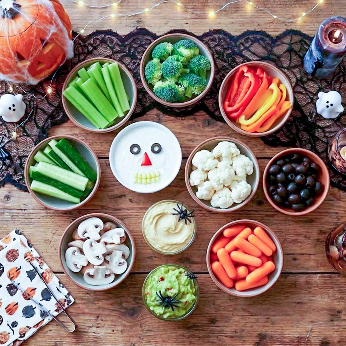 Bowls of celery, broccoli, bell pepper strips, cucumber, cauliflower, olives, mushrooms, and baby carrots with ranch, hummus, and guacamole.
