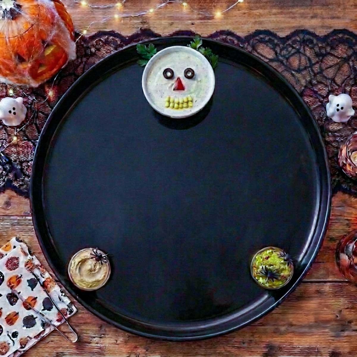 Empty black Halloween platter with a bowl of ranch dip decorated as a skull face and two smaller dip bowls at the bottom.