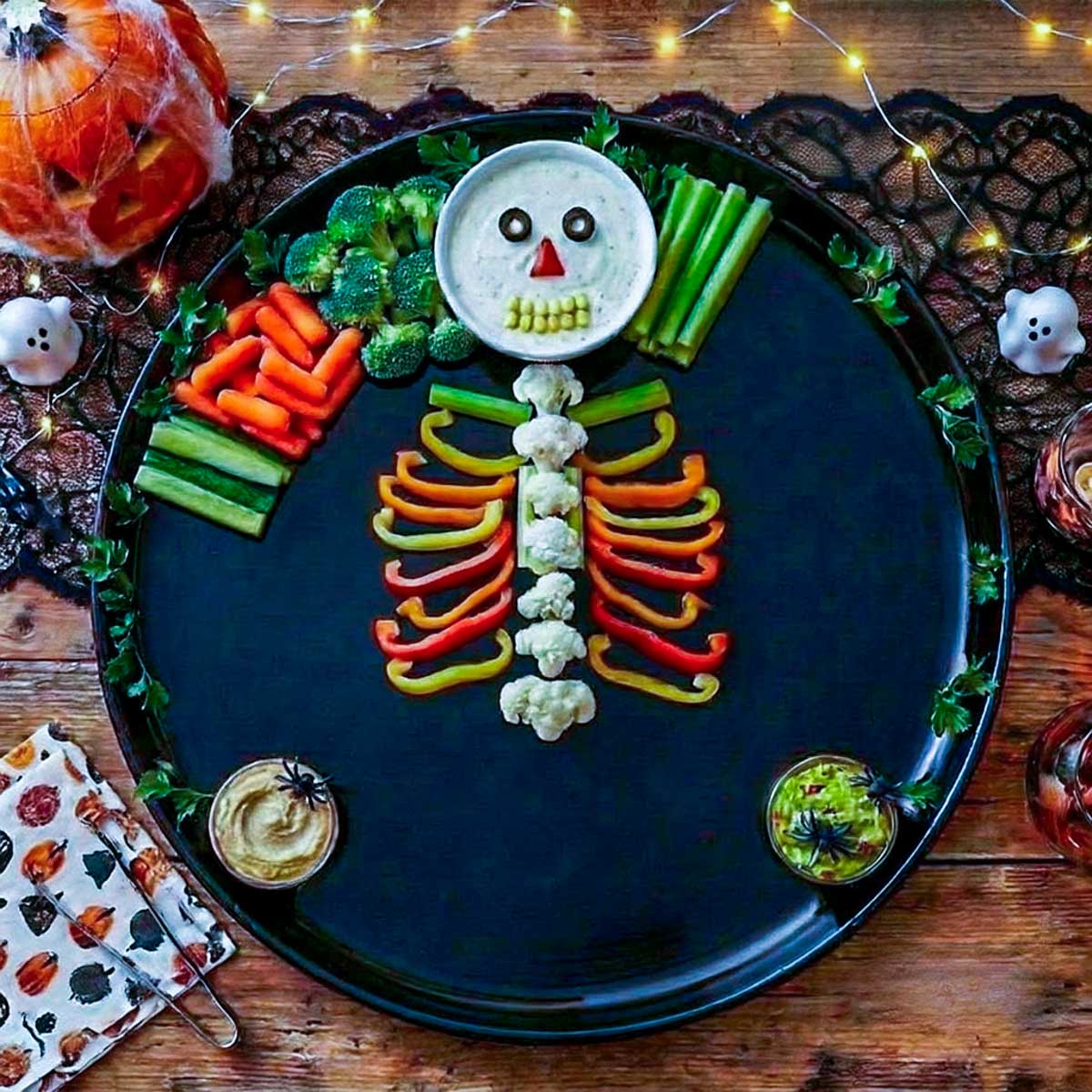 Cauliflower spine with red, yellow, and orange bell pepper ribs arranged on a black Halloween platter.
