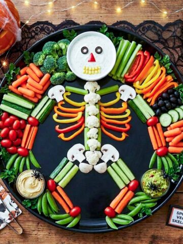 Halloween veggie tray arranged as a skeleton on a black platter with a ranch dip skull, bell pepper ribs, and cauliflower spine.