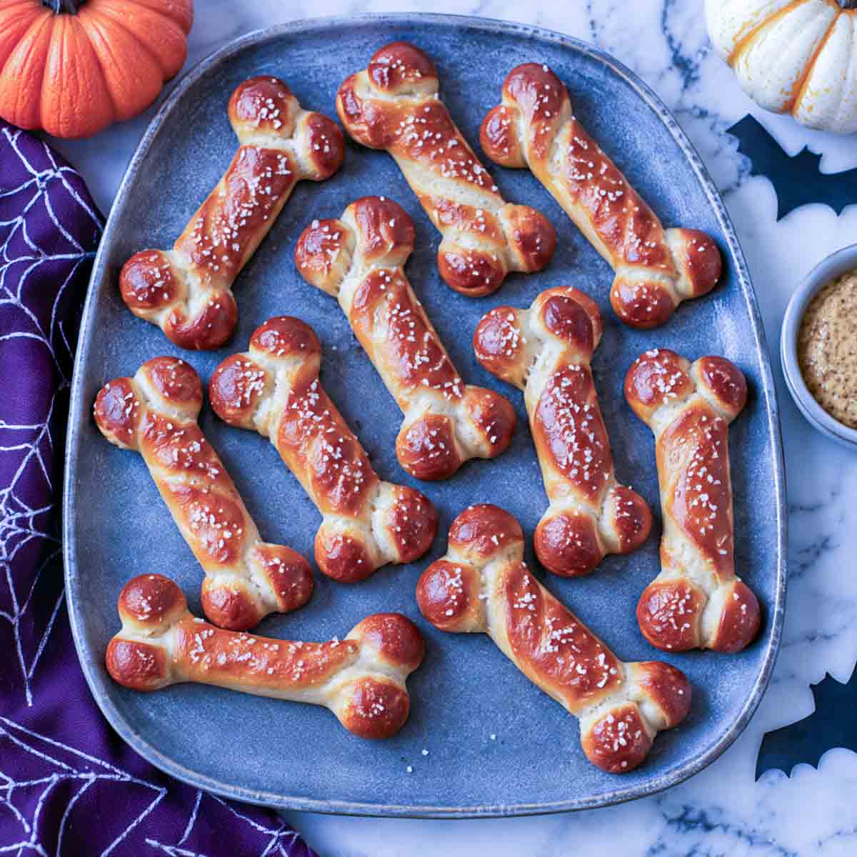 Soft pretzel bones with salted knobbed ends on a gray platter with a bowl of grainy mustard.