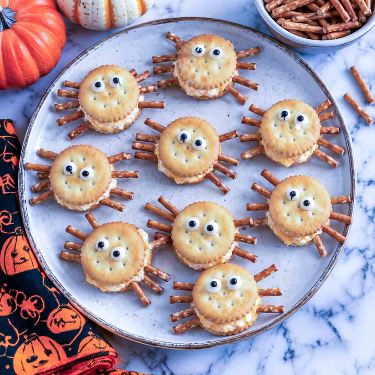 Spider crackers made from round butter crackers with cheese filling and pretzel stick legs on a speckled plate.