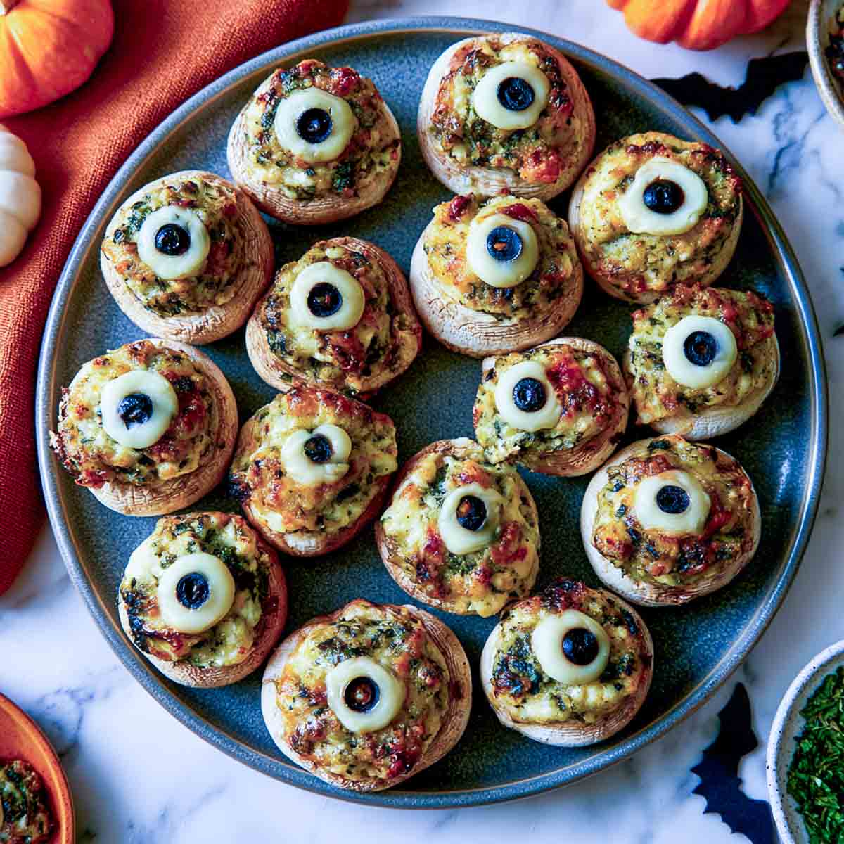 Stuffed mushroom eyeballs with spinach filling and mozzarella rounds with black olive pupils on a blue plate.